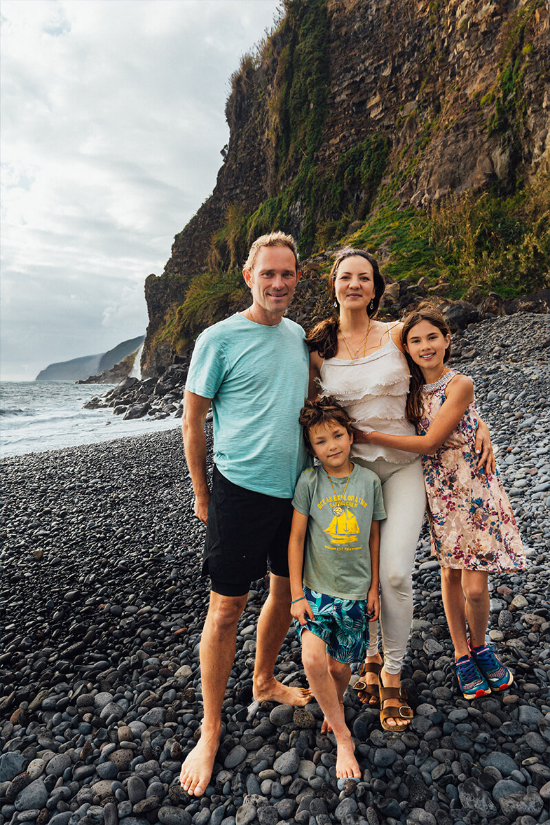 Familienfoto barfuß auf schwarzem Kiesstrand – natürliche und fröhliche Portraitaufnahme