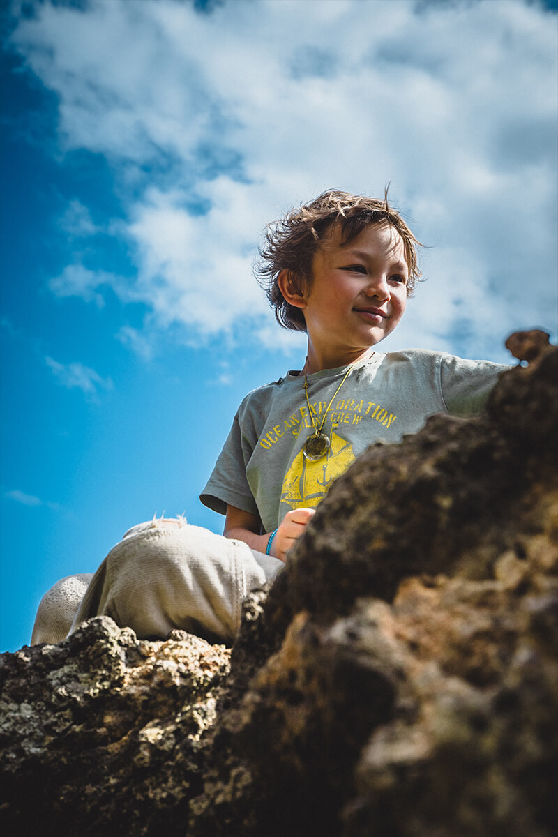 Junge sitzt auf Felsen unter blauem Himmel – natürliches Outdoor-Portrait auf Madeira